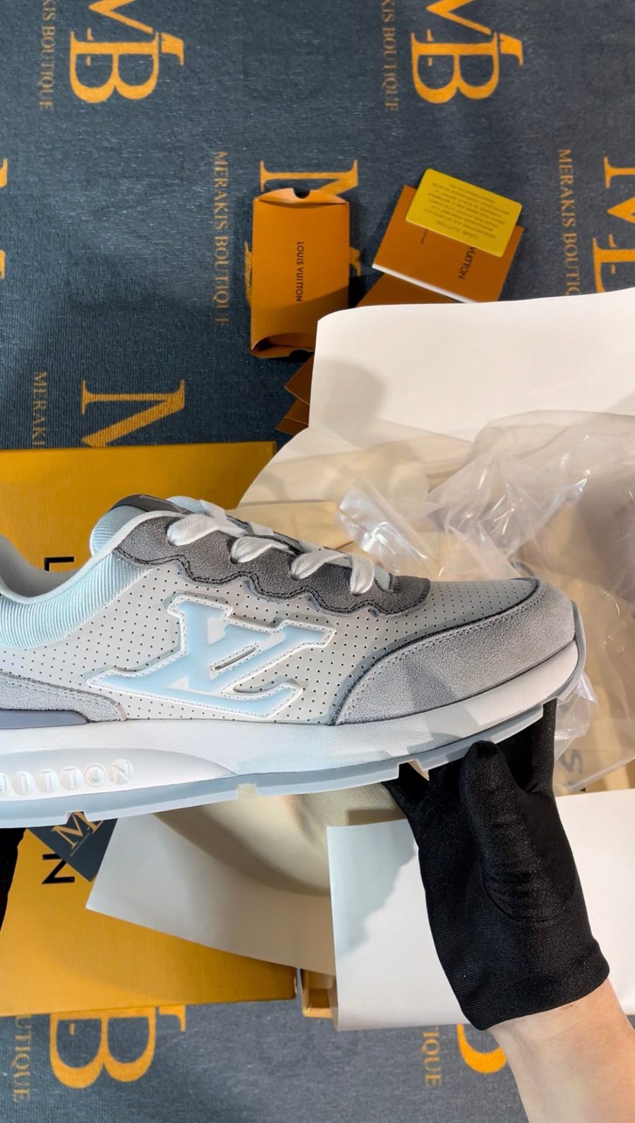 Grey and pale blue designer runner sneaker held in a gloved hand